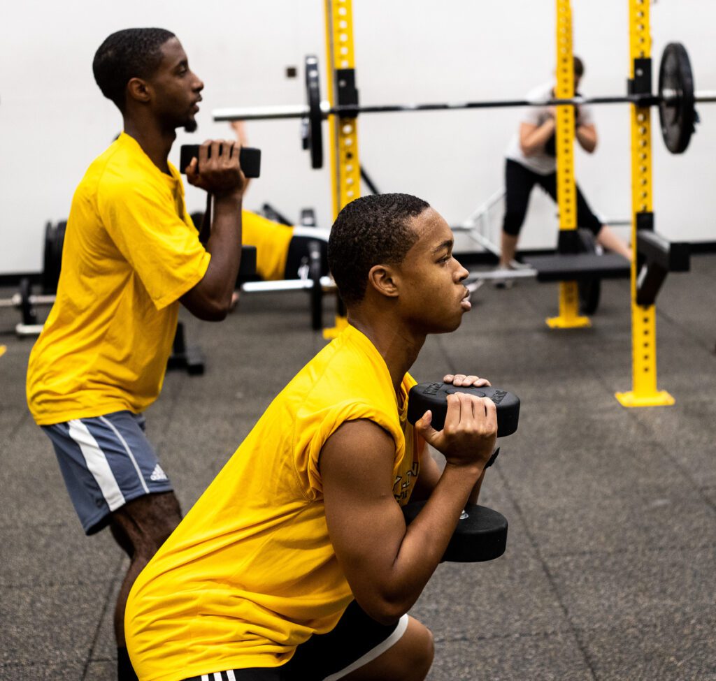 Two men work out at the Physical Activities Center with weights.
