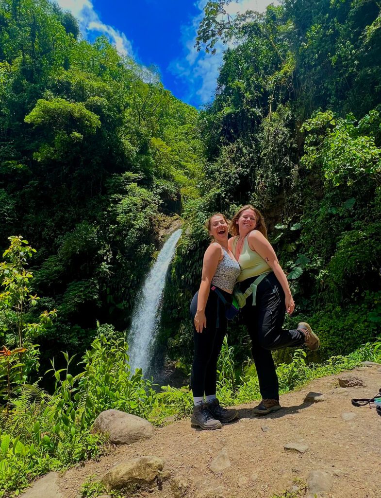 Two students stand together in front of a waterfall in Costa Rica, smiling.