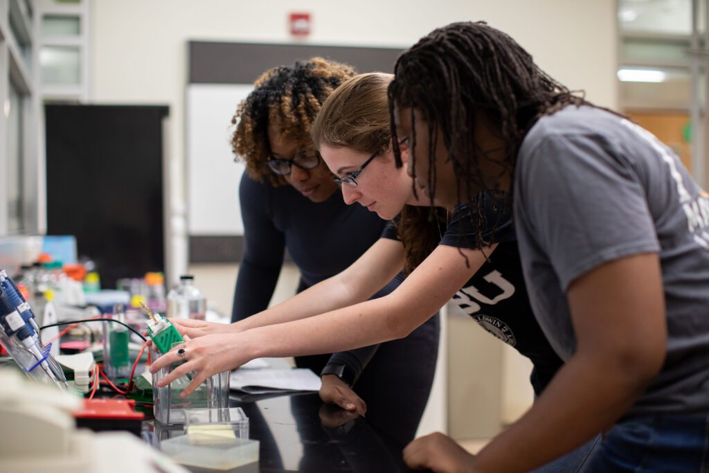 Three students work with equipment in a lab.
