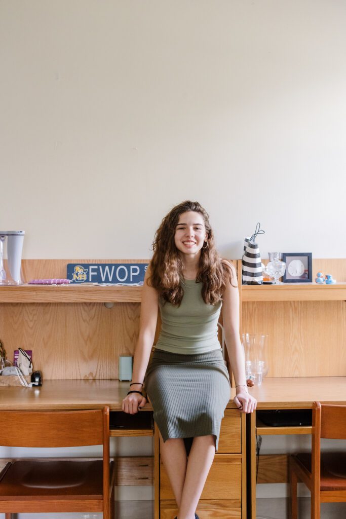 A student sits on the desk in her dorm and smiles.
