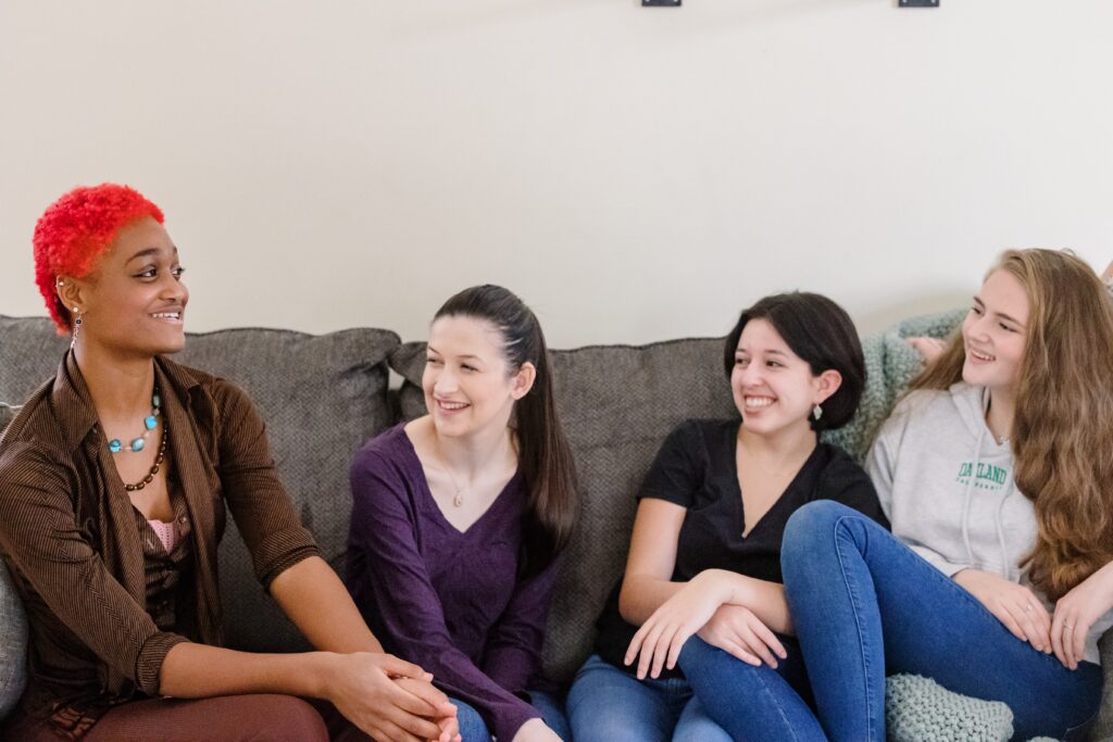 A group of PEG students sit on a couch, laughing.