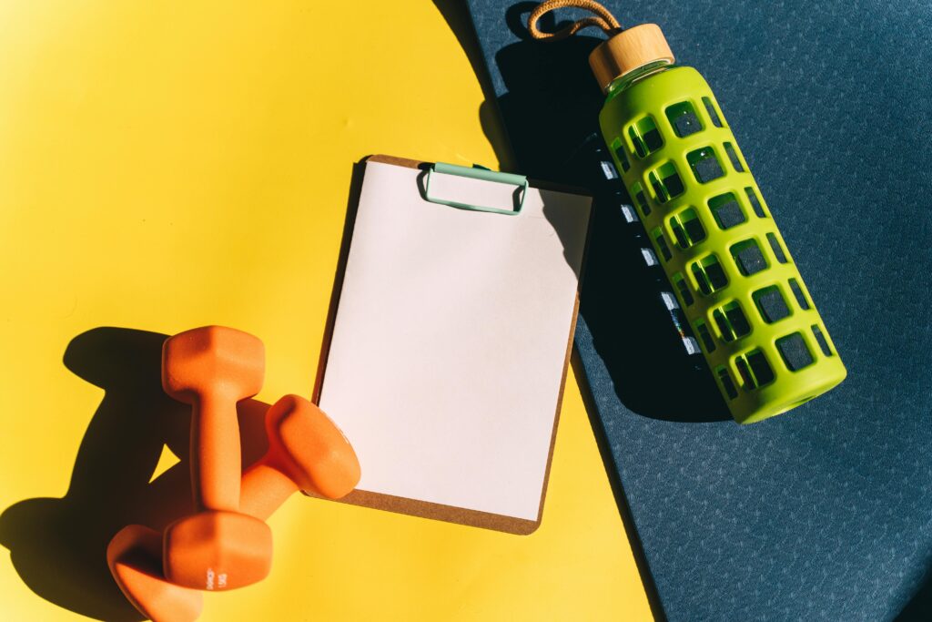 Weights, a water bottle, and a clipboard rest on an exercise mat.