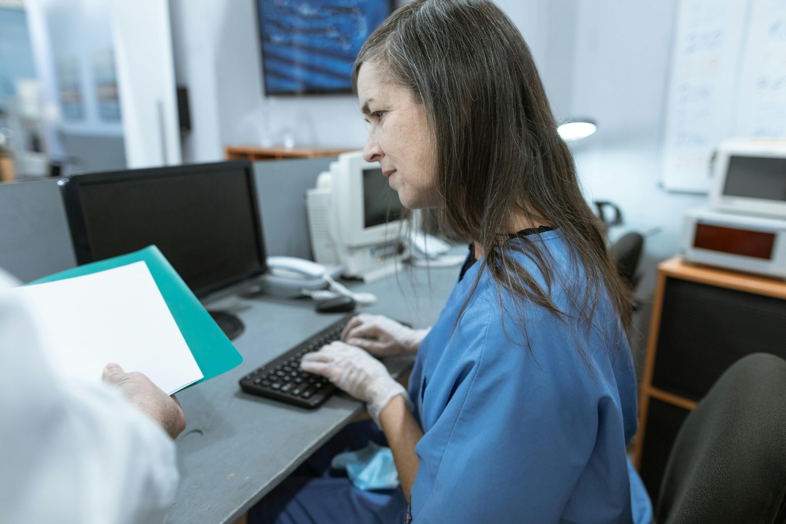 A nurse reads a report and types on a computer