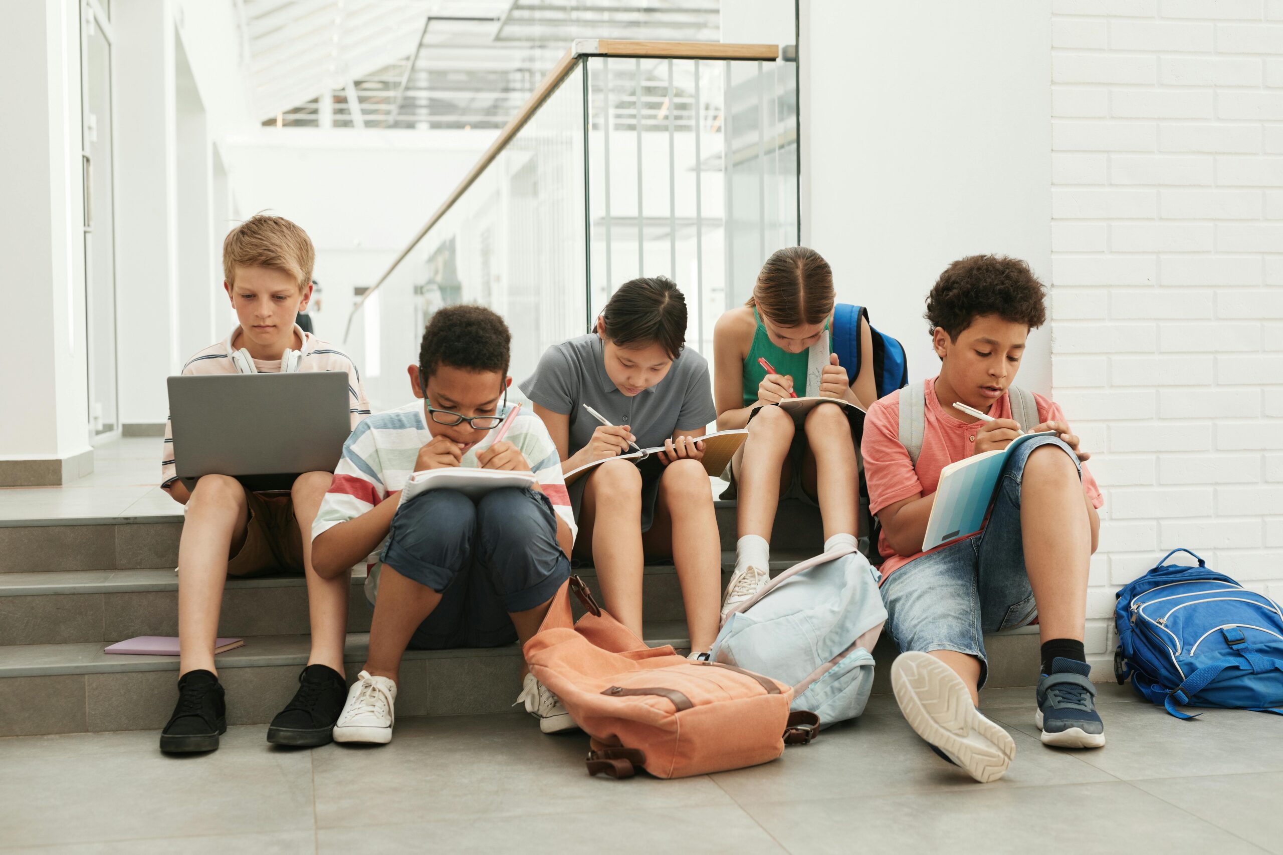 Middle school students sit on steps doing schoolwork