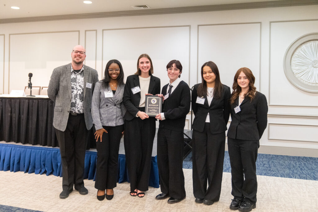 Students and a faculty member pose with a plaque